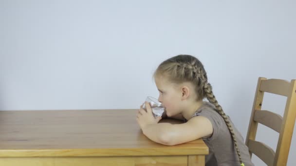 Little girl drinks water from a glass while — Stock video