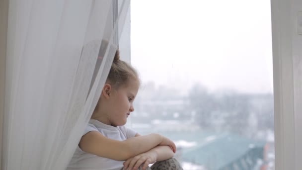 Smutný holčička dívá z okna, si myslí, že o něčem a odsuzuje to. — Stock video