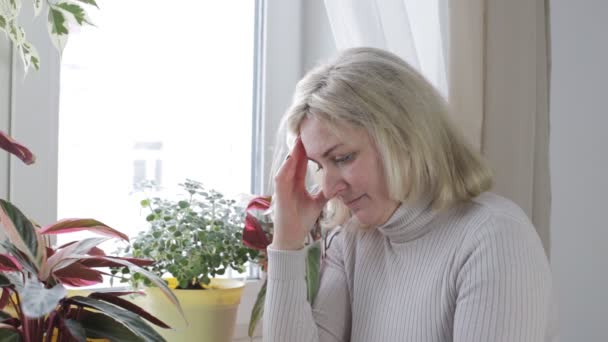 Žena sedí u okna obav tře její čelo a je nervózní — Stock video