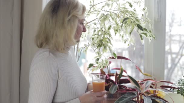 Frau blickt nachdenklich aus dem Fenster und trinkt Saft — Stockvideo