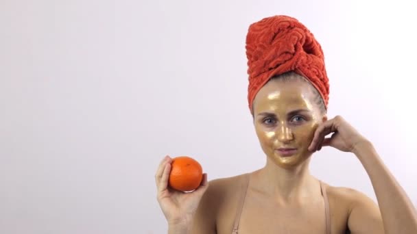 Flicka visar en gyllene mask på ansiktet jämfört med en orange frukt — Stockvideo