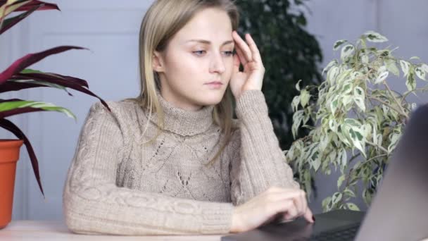 Menina Pensive senta-se em um laptop e escolhe algo. Ambiente doméstico ocasional — Vídeo de Stock