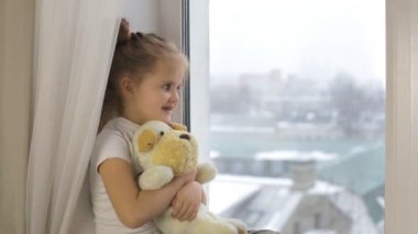 Küçük kız kenarında oturan ve tutmak bir yumuşak oyuncak