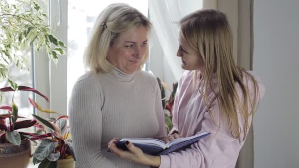Мати і дочка дивляться на блокнот з нотатками і розмовляють — стокове відео