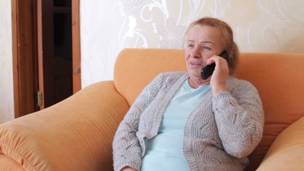 Бабушка разговаривает по телефону, сидя в кресле — стоковое видео