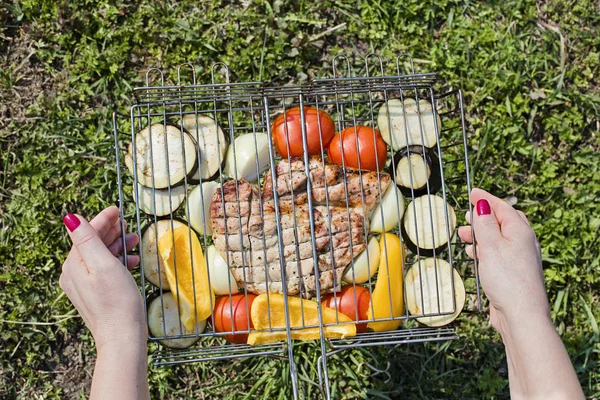 Female hands holding appetizing vegetables and pork steak on a wire rack — Stock Photo, Image
