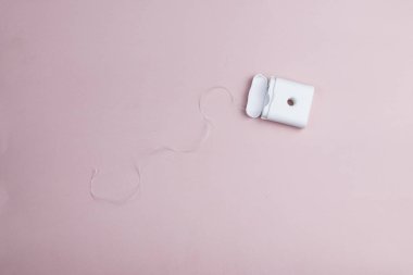 Pembe arka plan üzerinde beyaz plastik bir kutu içinde açık diş ipi