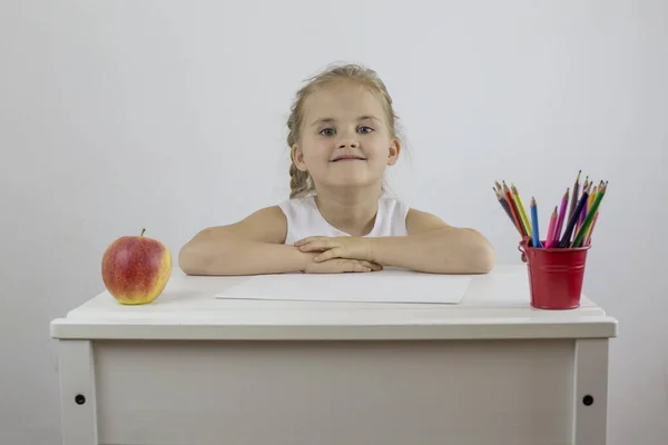 Задоволена маленька дівчинка сидить за столом з олівцями і стигле яблуко — стокове фото