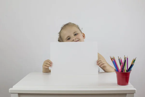 Dziewczynka siedzi przy biurku i trzyma białą kartkę papieru — Zdjęcie stockowe