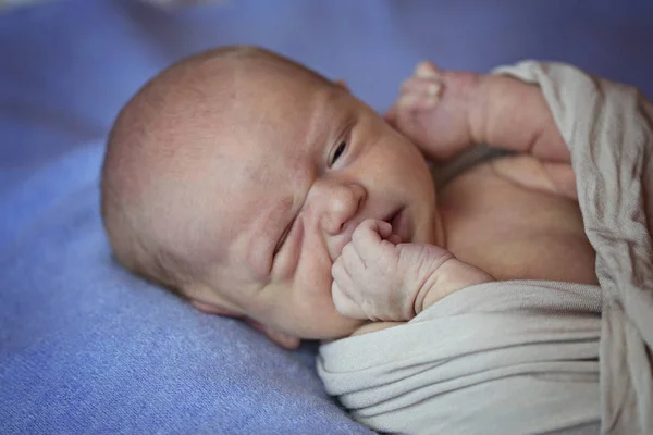 Una niña recién nacida se muerde los dedos y mira con un ojo —  Fotos de Stock