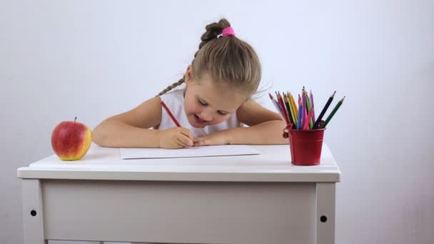 Lány egy preschooler ül az íróasztalon, és szorgalmasan végzi a feladatot — Stock videók