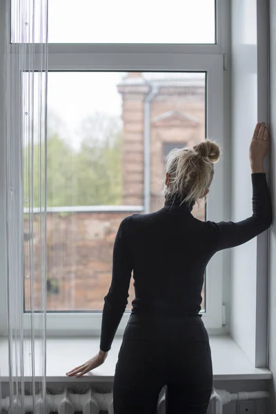 Sırtıyla duran kadın pencereden dışarı bakıyor.