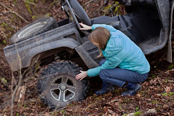 Uma mulher verifica os pneus de um buggy que rolou abaixo de uma montanha em uma vala — Fotografia de Stock