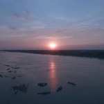 Antena: fly powrót ujawniając bambus most nad rzeką o zachodzie słońca, z sylwetkami osób pływanie wokół zacumowane łodzie