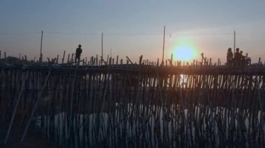 Hava kaydırma atış bir bambu üzerinde çalışan bir genç çocuk bir nehir üzerinde günbatımında köprü.