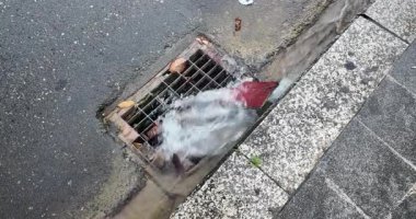 Bir sokak oluğundan aşağı, güçlü bir fırtına suyu akıntısı, metal bir kanalizasyona hücum ederken yaprakları ve diğer kalıntıları taşır..