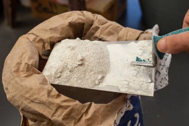 Kese kağıdından bir malanın üzerinde macun gibi çimento tutan bir erkek.  