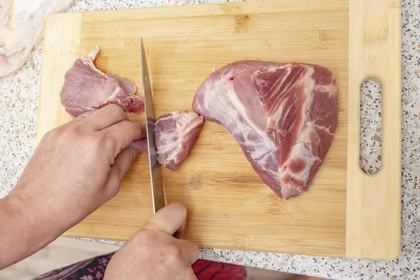 Kadın elleri odun kesme tahtasında çiğ domuz eti kesiyor. 