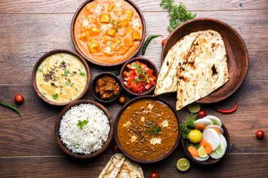 Assorted indian food for lunch or dinner, rice, lentils, paneer, dal makhani, naan, chutney, spices over moody background. selective focus clipart