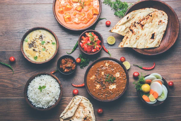 Assorted indian food for lunch or dinner, rice, lentils, paneer, dal makhani, naan, chutney, spices over moody background. selective focus