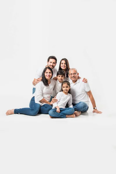 Indian family sitting over white background. senior and young couple with kids wearing white top and blue jeans. selective focus