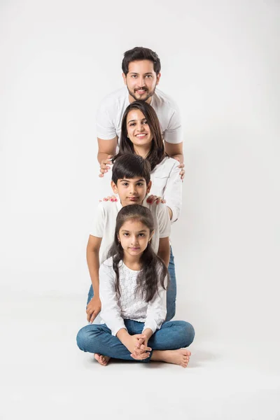 happy Indian family of 4 standing isolated over white background. Young couple with kids wearing white top and blue jeans. selective focus