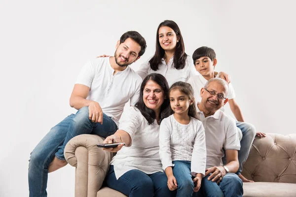 Indian family watching TV while sitting on sofa or couch over white background