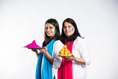 Anne ve kızı Holi oynuyorlar, ellerinde tatlı laddu ve renklerle dolu tabakları tutuyorlar. beyaz arkaplan üzerinde izole