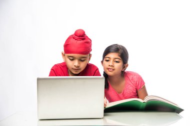 Indian sikh/Punjabi  boy and girl studying with books and laptop computer at study table clipart