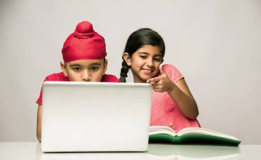 Hint Sih/Punjabi çocuk ve kitap ve dizüstü bilgisayar çalışma masasında ile okuyan kız