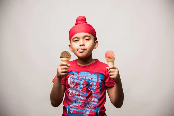 Indian Sikh/punjabi small boy eating ice cream in cone, isolated over white background