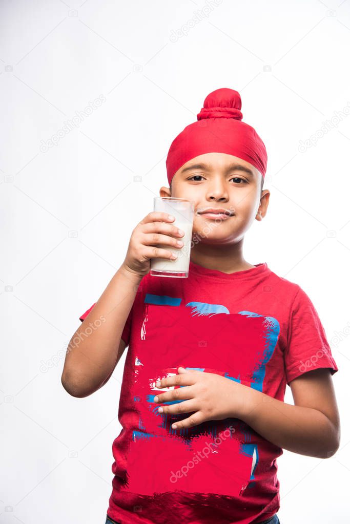 Indian Sikh/punjabi small boy holding a glass full of milk, isolated over white background