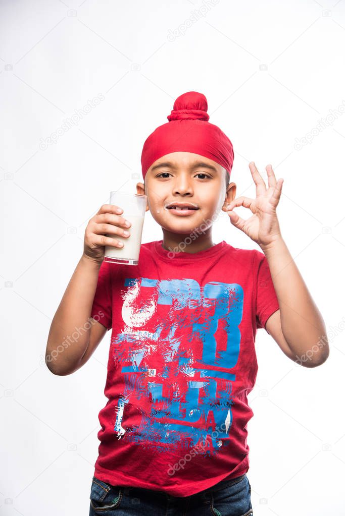 Indian Sikh/punjabi small boy holding a glass full of milk, isolated over white background
