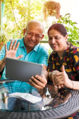 Hint/Asya kıdemli çift görüntülü kanepe veya evde, bahçede seçici odak otururken tablet/bilgisayarda sohbet