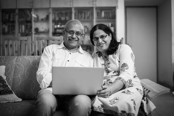 Senior Indian/asian couple accounting, doing home finance and checking bills with laptop, calculator and money while sitting at home garden