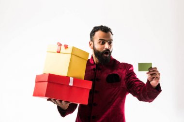 Sakallı, elinde hediye kutusu ve boş bir kart olan genç ve mutlu Hintli bir adam geleneksel giysiler / sherwani giyer, beyaz arka planda durur.