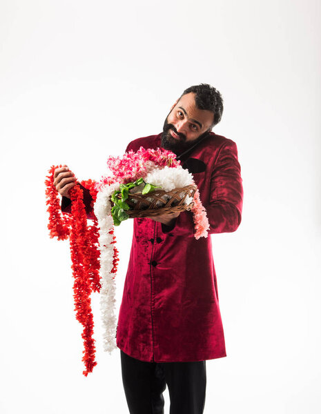 Indian man holding flower garland / series for decoration on diwali/ wedding or festivals while wearing traditional cloths / sherwani , standing isolated over white background