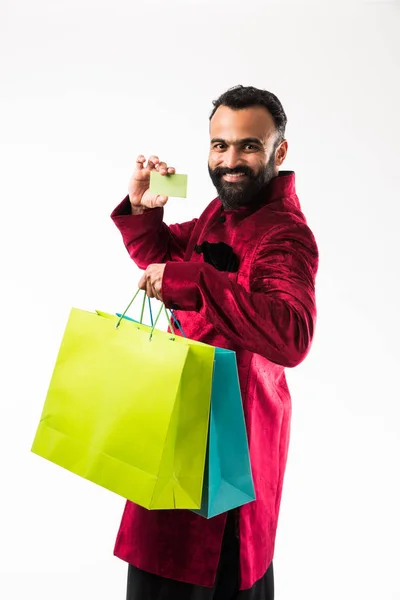 赤い伝統的な服を着て買い物をしている間にカードを見せるインド人男性 白い背景の上にカラフルな紙袋で孤立した立っている — ストック写真