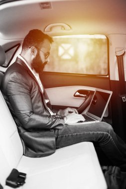 Araba içinde dizüstü bilgisayar ve telefon kullanarak Hint / asyalı genç işadamı, seçici odak