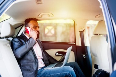 Araba içinde dizüstü bilgisayar ve telefon kullanarak Hint / asyalı genç işadamı, seçici odak