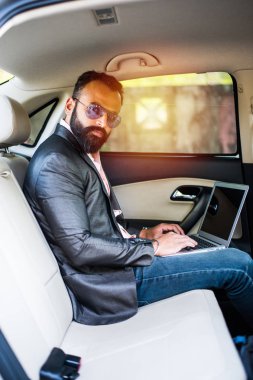 Araba içinde dizüstü bilgisayar ve telefon kullanarak Hint / asyalı genç işadamı, seçici odak