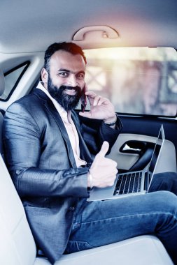 Araba içinde dizüstü bilgisayar ve telefon kullanarak Hint / asyalı genç işadamı, seçici odak