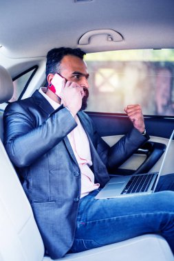 Araba içinde dizüstü bilgisayar ve telefon kullanarak Hint / asyalı genç işadamı, seçici odak