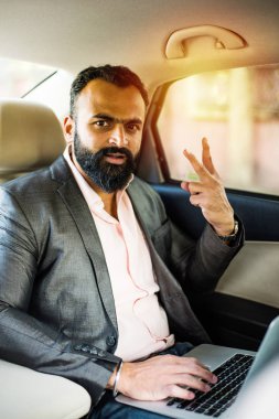 Araba içinde dizüstü bilgisayar ve telefon kullanarak Hint / asyalı genç işadamı, seçici odak