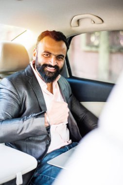 Araba içinde dizüstü bilgisayar ve telefon kullanarak Hint / asyalı genç işadamı, seçici odak