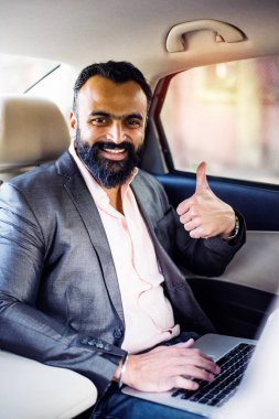 Araba içinde dizüstü bilgisayar ve telefon kullanarak Hint / asyalı genç işadamı, seçici odak