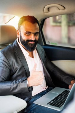 Araba içinde dizüstü bilgisayar ve telefon kullanarak Hint / asyalı genç işadamı, seçici odak