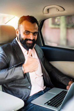 Araba içinde dizüstü bilgisayar ve telefon kullanarak Hint / asyalı genç işadamı, seçici odak