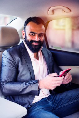 Araba içinde akıllı telefon kullanan Hint / asyalı genç işadamı, seçici odak