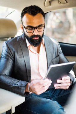 Arka koltukta otururken Tablet bilgisayar/sekme kullanan Hintli/asyalı genç işadamı, seçici odak